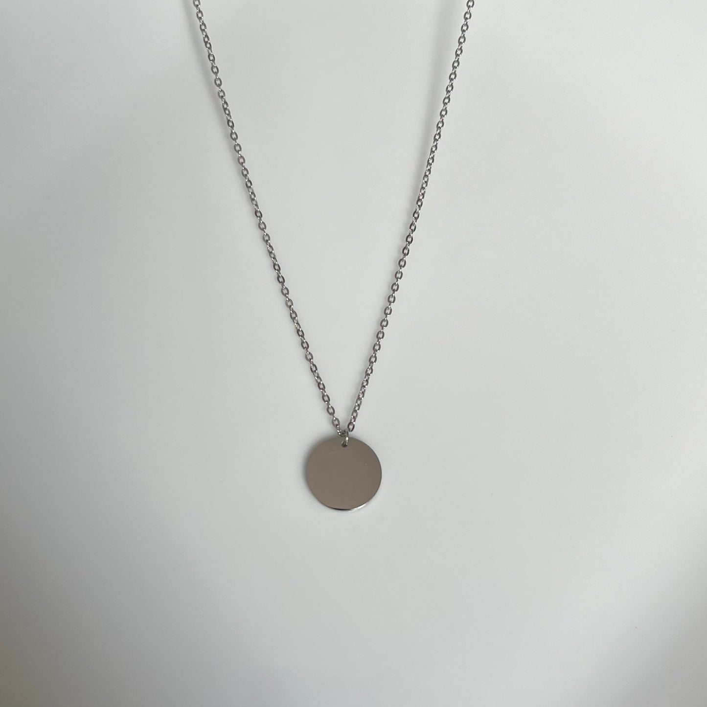 Elegant stainless steel disc pendant necklace with a shiny, polished disc on a chain.