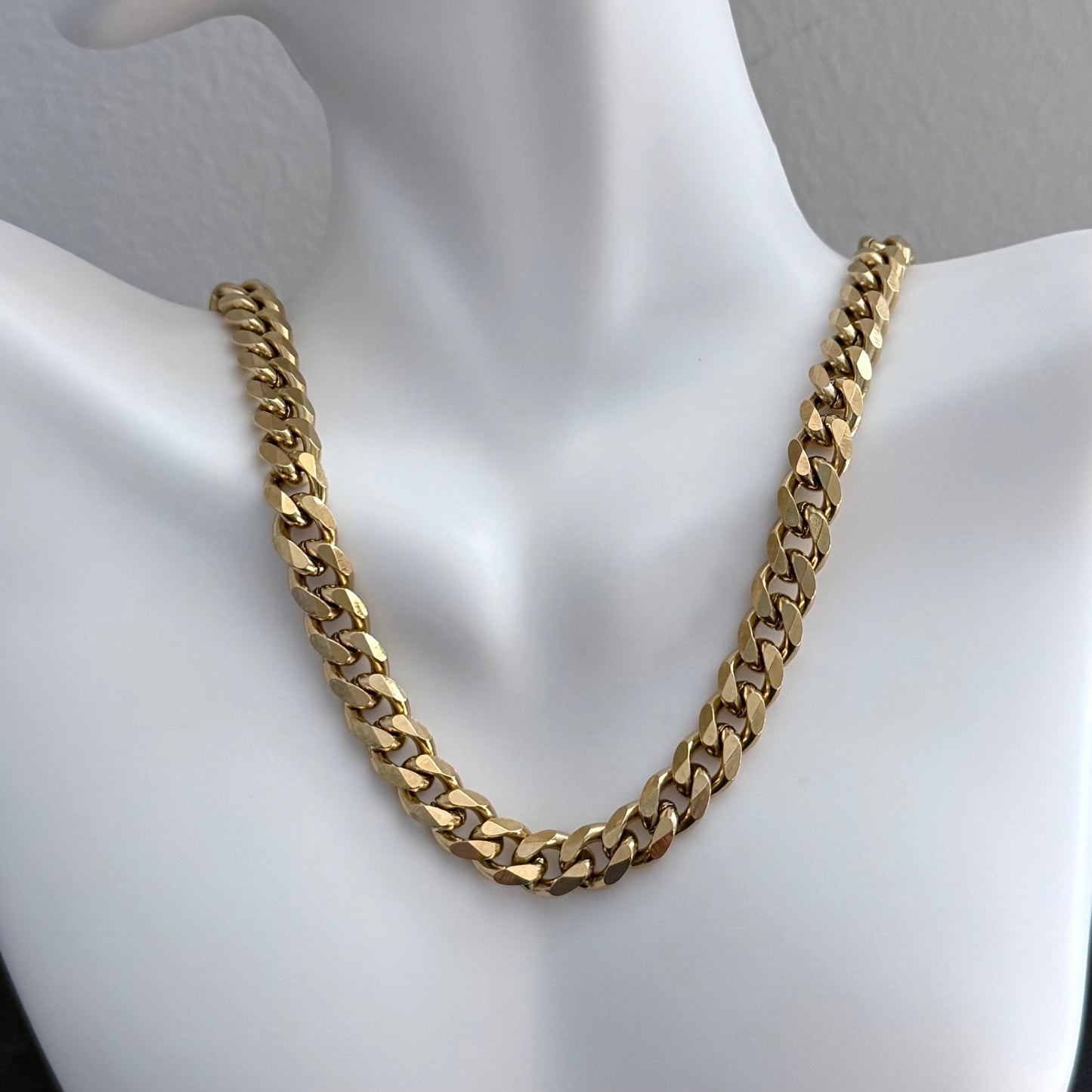 Gold chain Cuban necklace on a mannequin neck against a neutral background