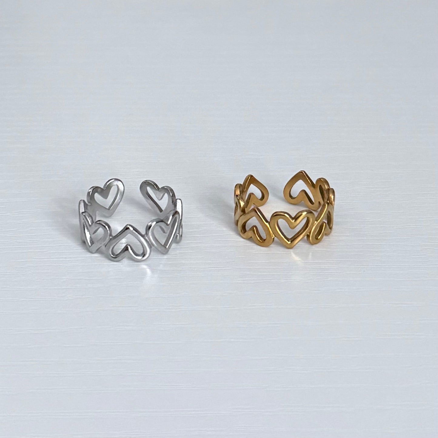 Two heart-shaped rings, one silver and one gold, on a light gray background.