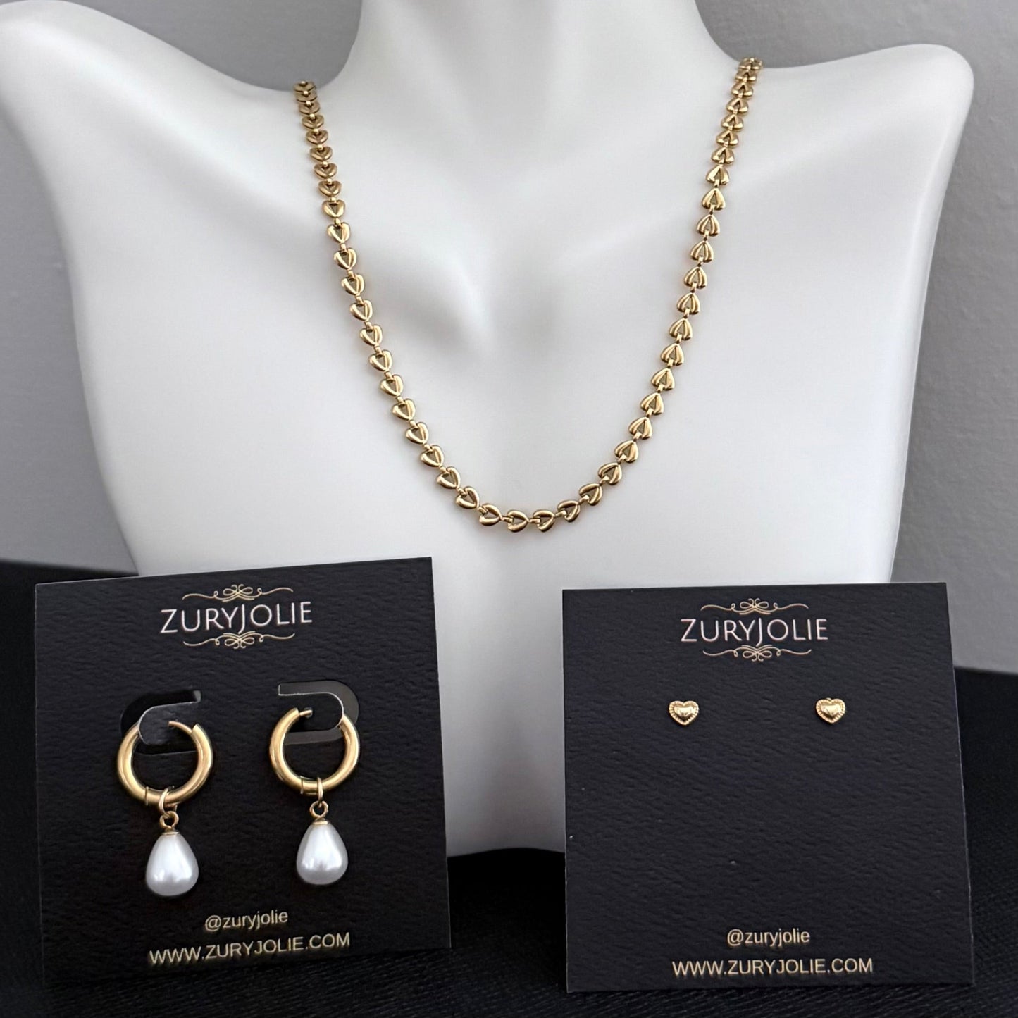 Gold necklace and earrings on a mannequin with ZuryJolie branding.