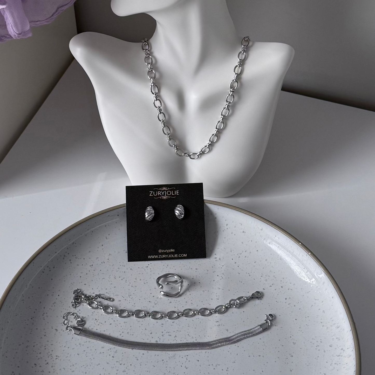 Silver jewelry set including necklace, earrings, and ring on a mannequin bust and plate.