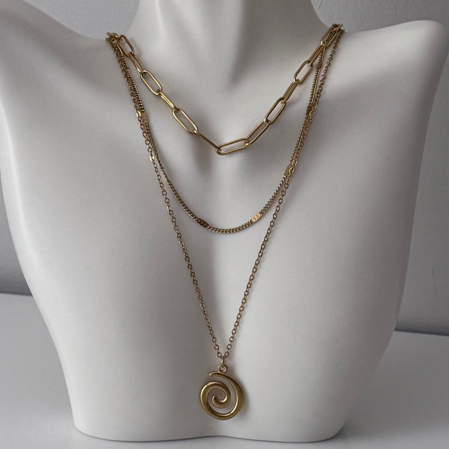 Gold chain necklace with a spiral pendant on a mannequin bust.