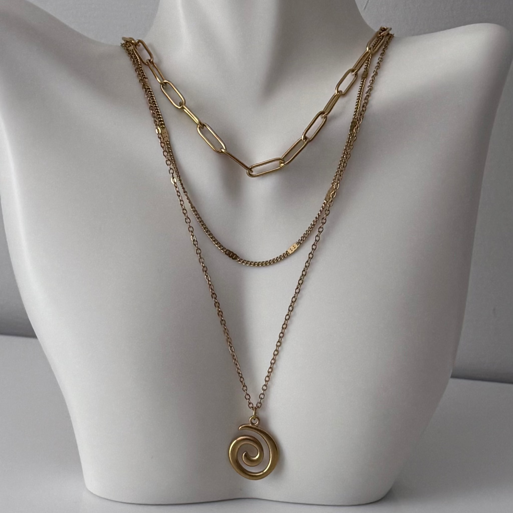 Gold chain necklace with a spiral pendant on a mannequin bust.