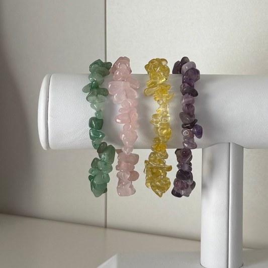 Set of four crystal chip bracelets in green, pink, yellow, and purple on a white cylindrical stand.
