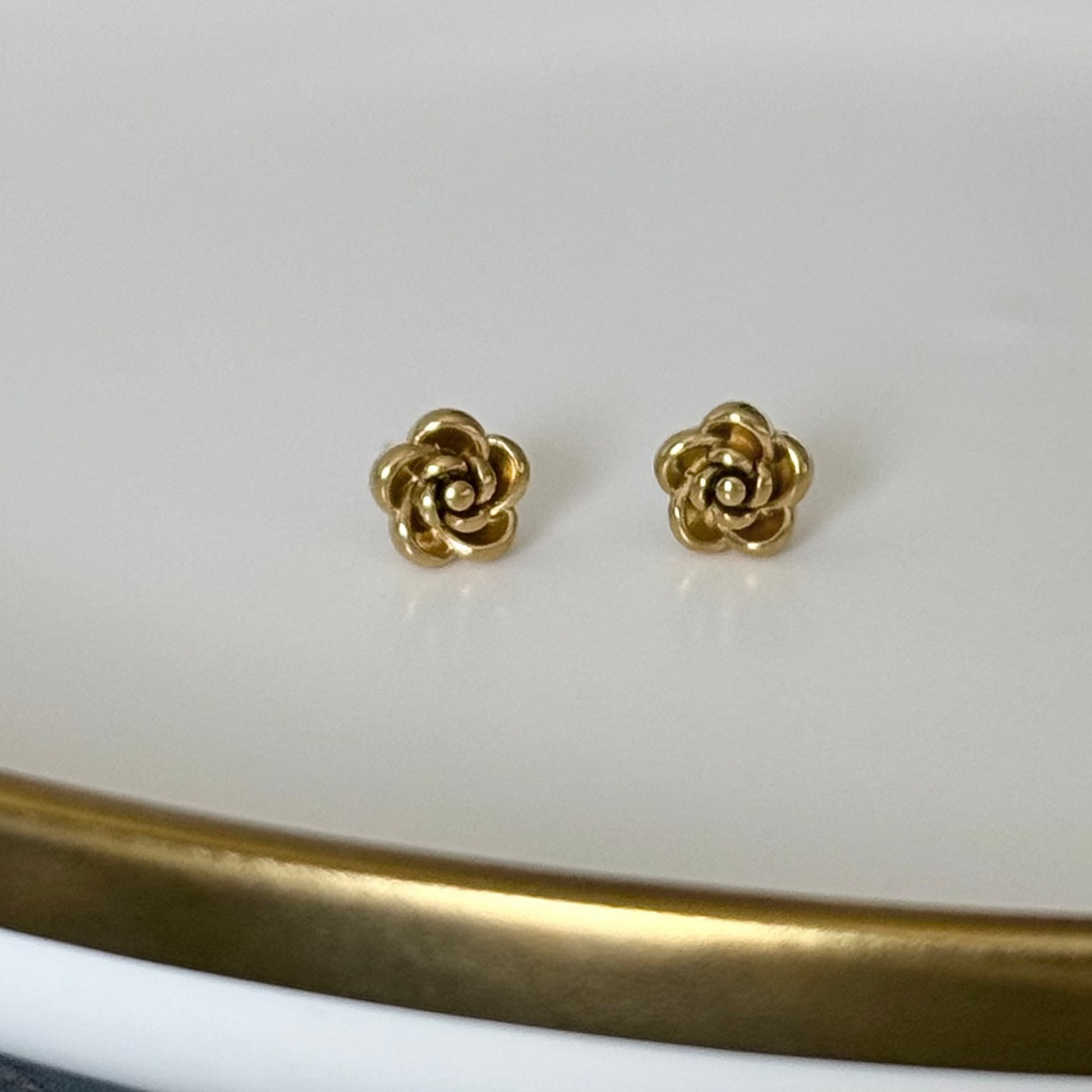 Gold rose-shaped earrings on a white surface with a gold rim.