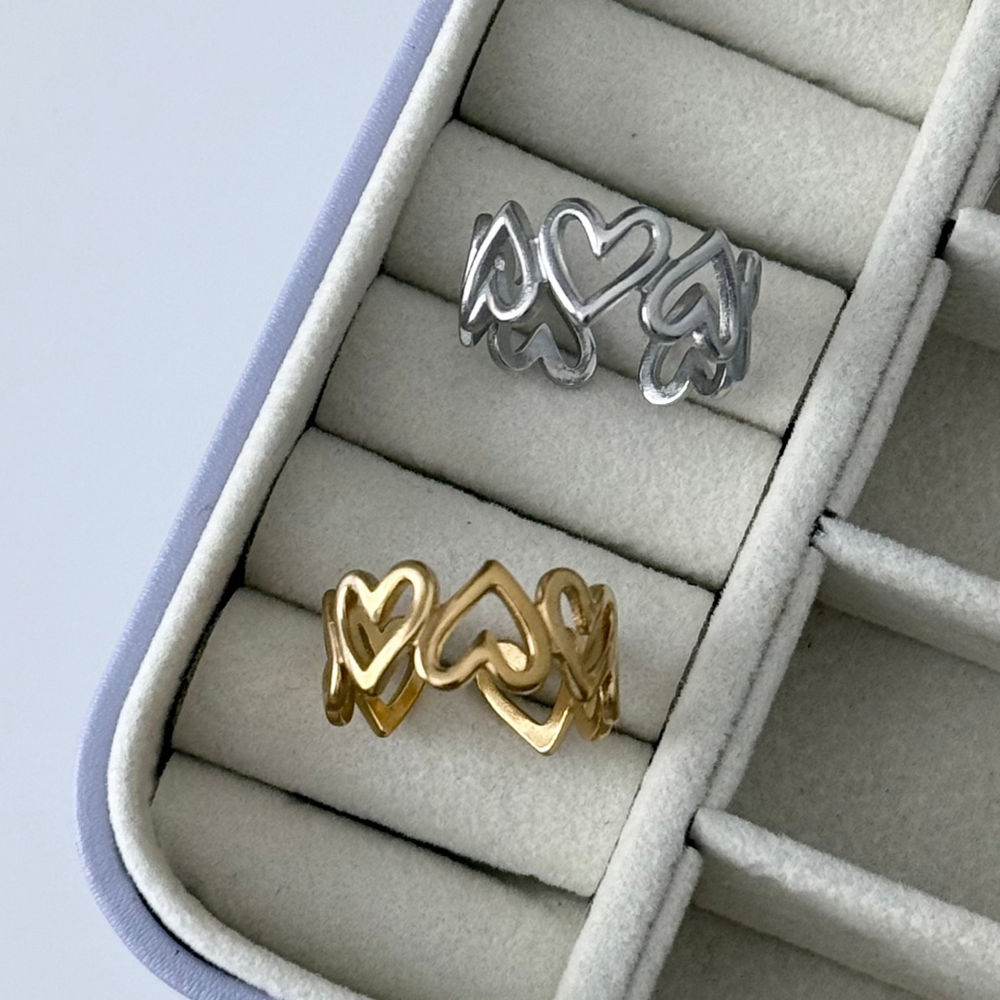 Two heart-shaped rings, one gold and one silver, in a jewelry box.