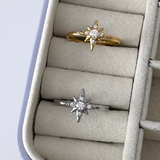 Two star-shaped rings, one gold and one silver, in a jewelry box.