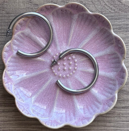 Pink ceramic dish with floral design holding metal earrings on a wooden surface