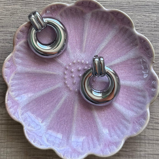 Silver hoop earrings on a pink ceramic dish with a floral design.