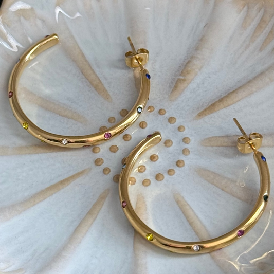 Gold hoop earrings with embedded stones on a textured white surface