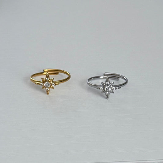 Two star-shaped rings, one gold and one silver, on a light gray background.
