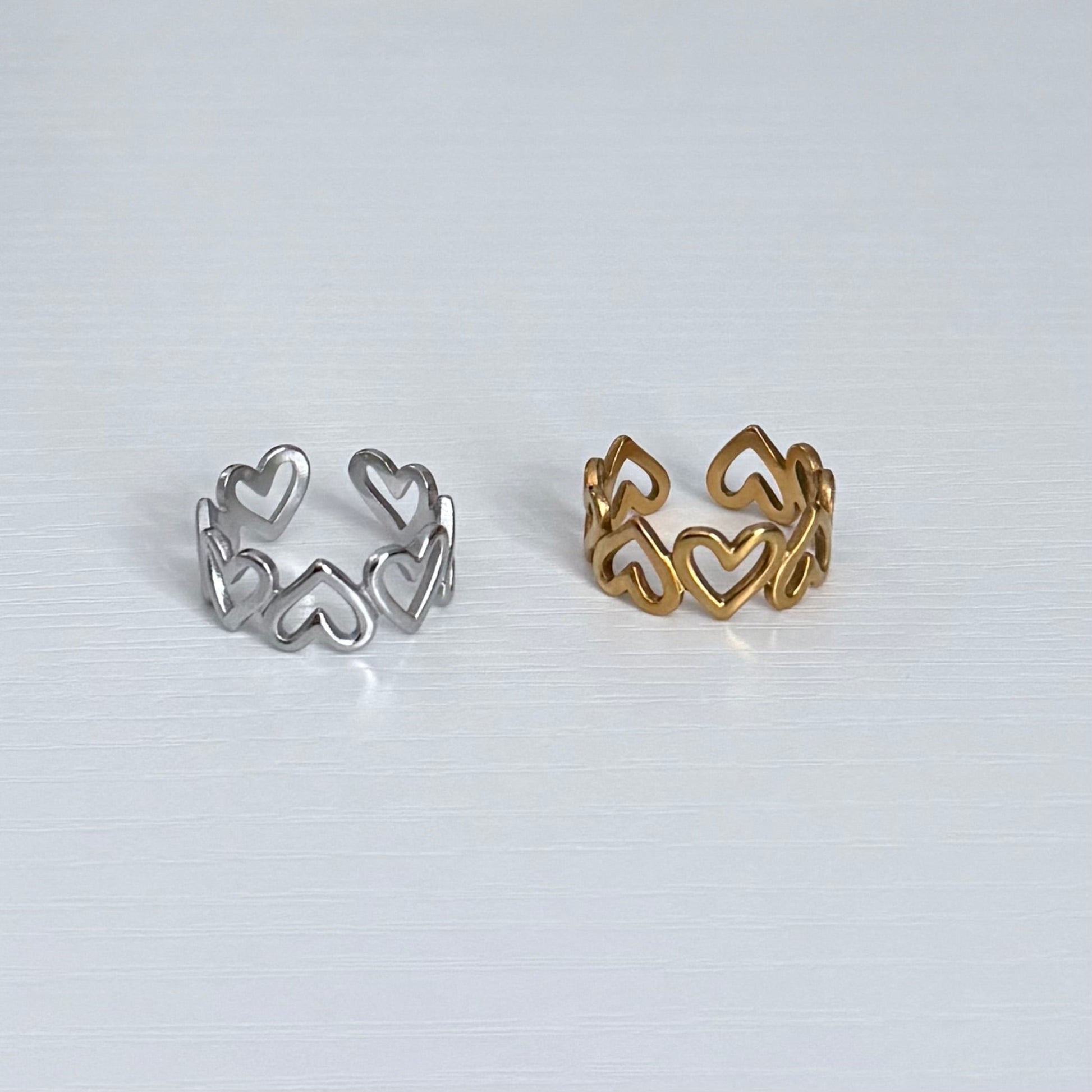 Two heart-shaped rings, one silver and one gold, on a light gray background.