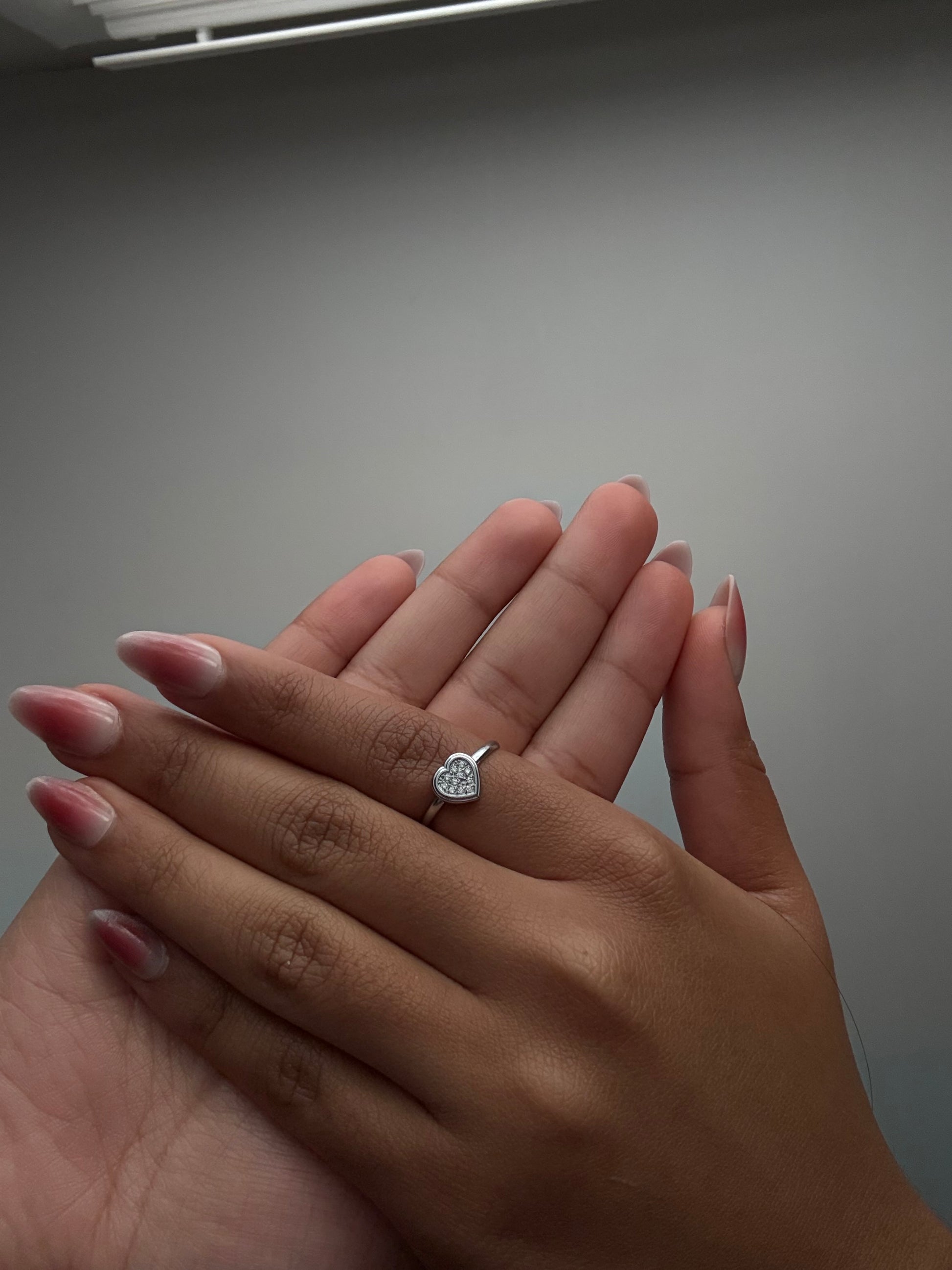 Close-up of a hand wearing a silver ring with a heart design on a neutral background