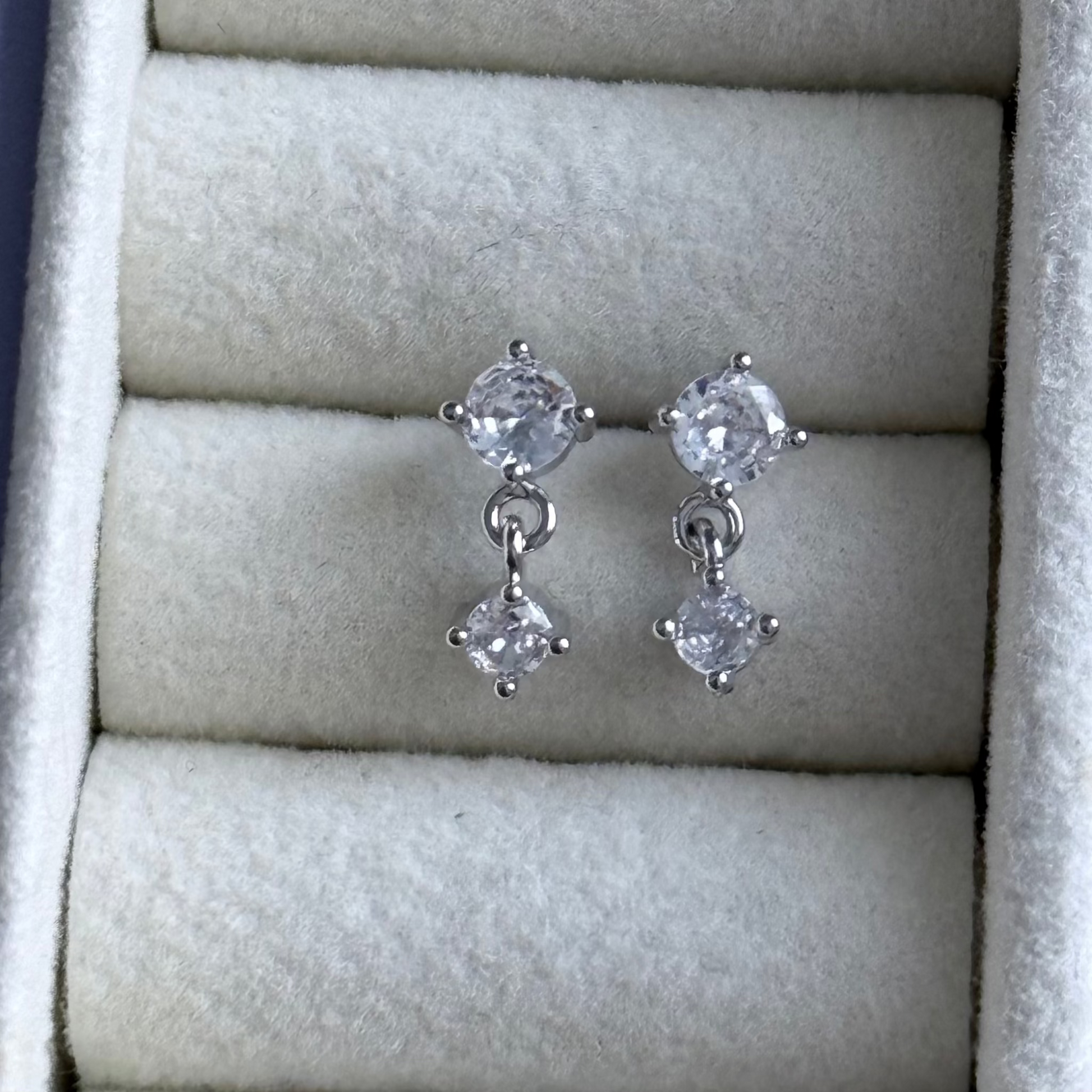 Pair of silver earrings with clear gemstones on a textured surface