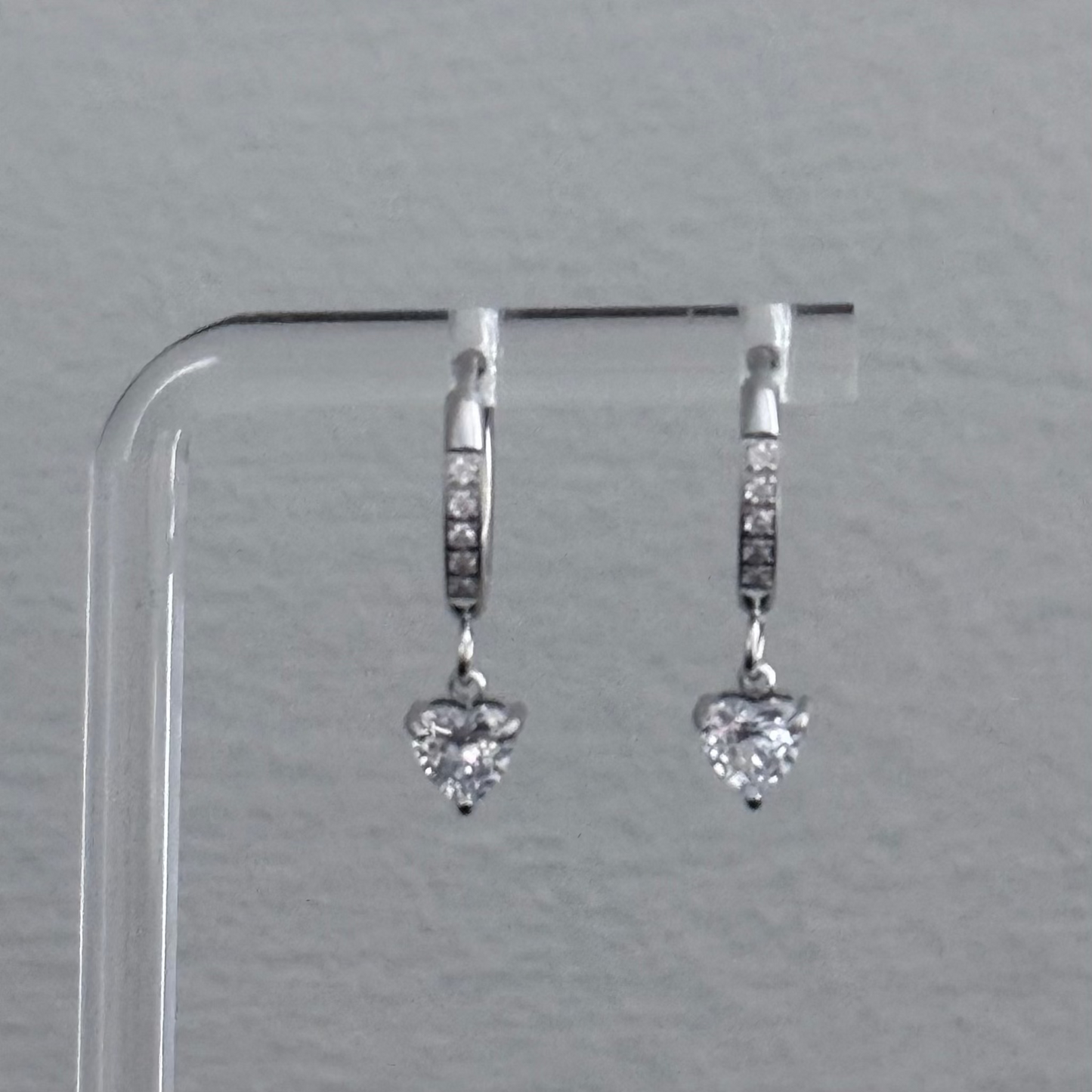 Heart-shaped diamond earrings on a clear stand against a gray background