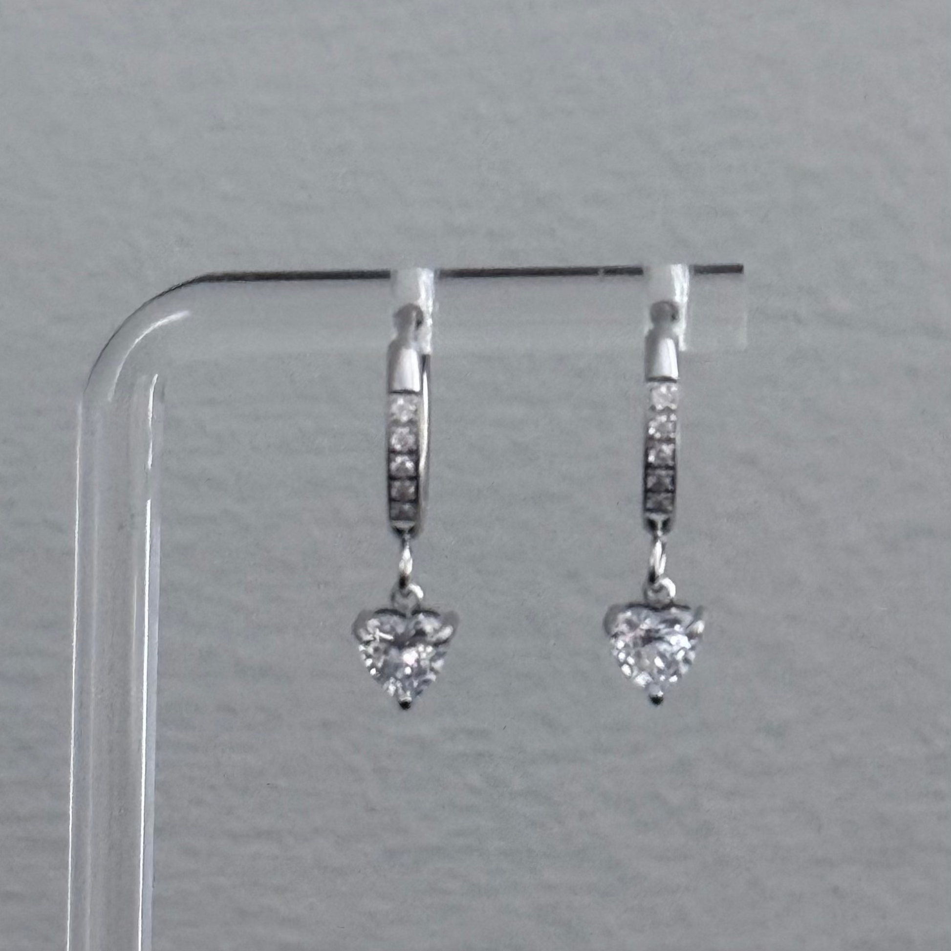 Heart-shaped diamond earrings on a clear stand against a gray background
