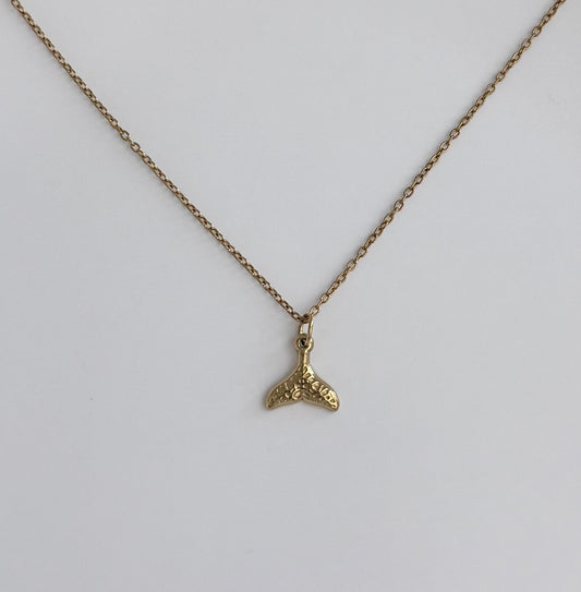 A gold chain necklace with a small textured gold whale tail pendant, displayed against a clean white background.
