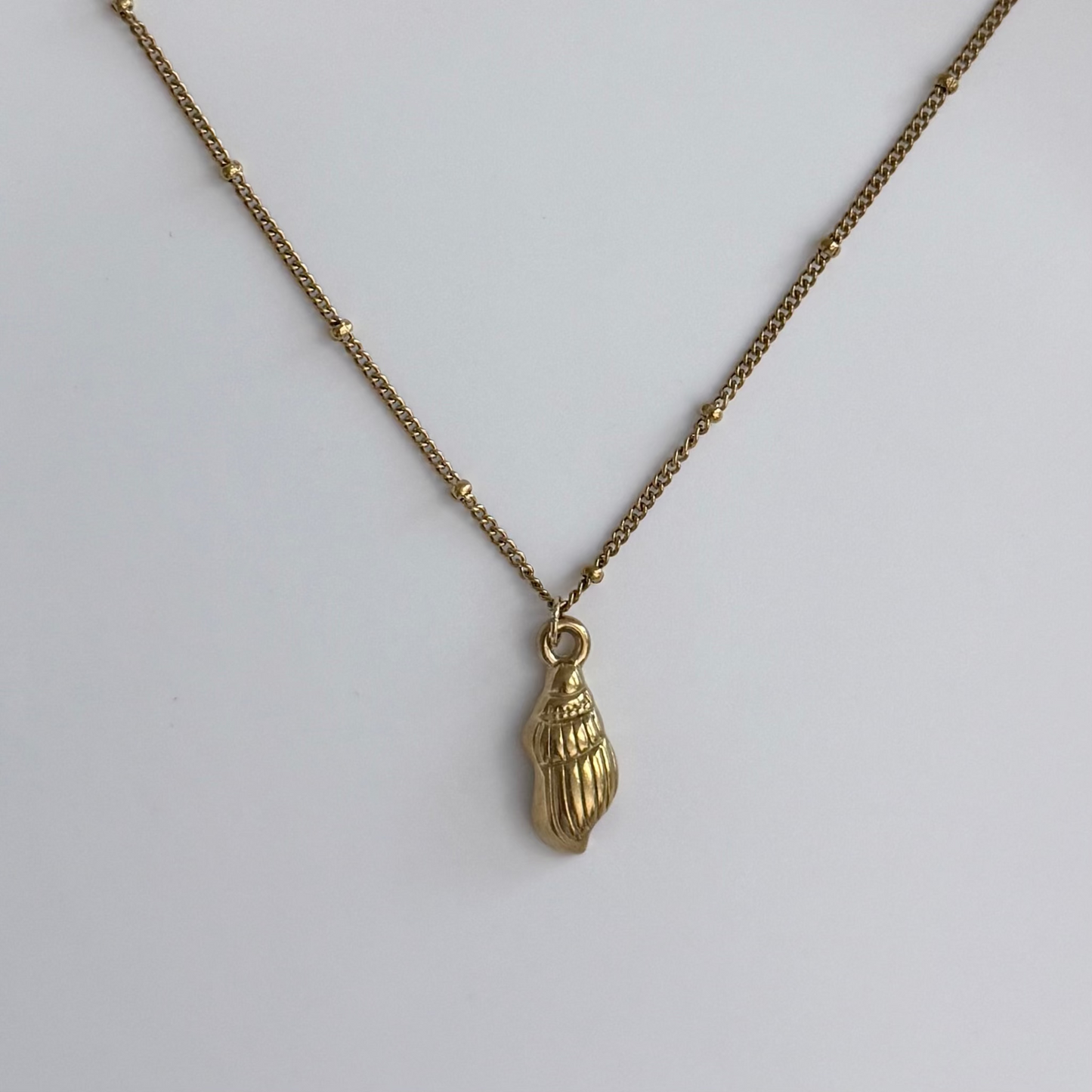 A gold-toned necklace featuring a textured, shell-like pendant, displayed on a clean, light gray background.