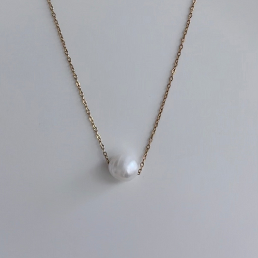 A delicate gold chain necklace featuring a single, irregular white baroque pearl pendant, displayed against a clean, light gray background.