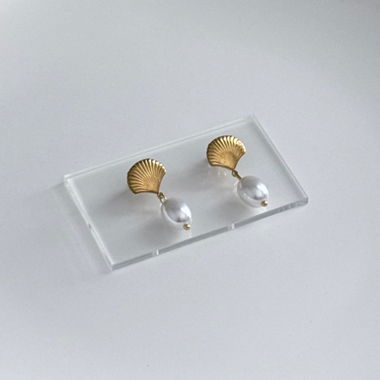 A pair of gold and pearl drop earrings displayed on a clear acrylic stand against a light gray background.