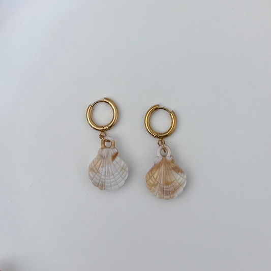 A pair of gold hoop earrings with dangling seashell charms, displayed on a clean, light gray background.