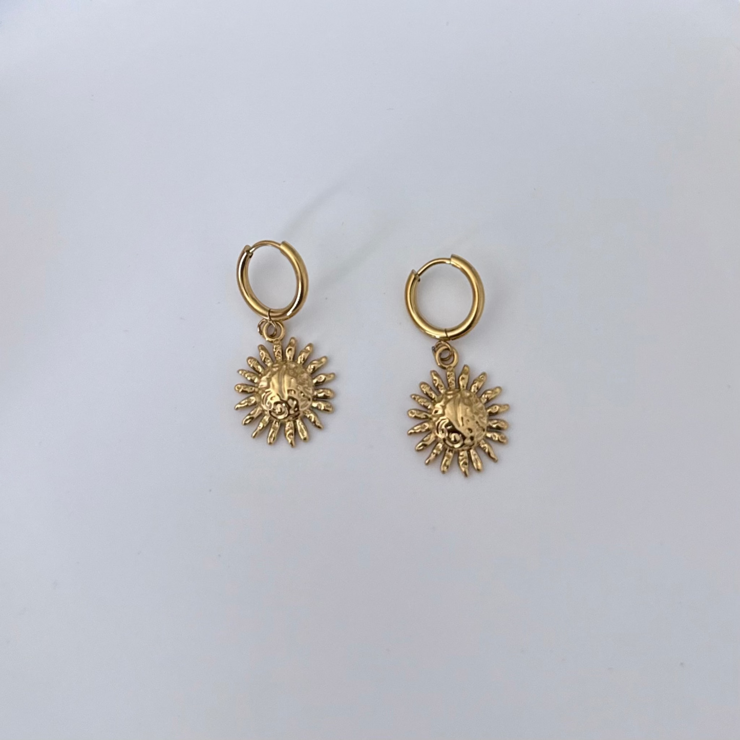 A pair of gold-toned dangle earrings featuring small hoop tops and textured sunburst charms, displayed on a clean white background.