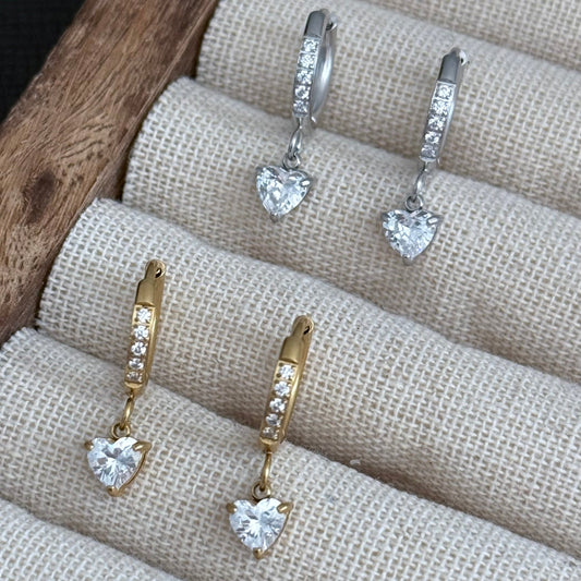 Pair of gold and silver heart-shaped earrings on a textured surface.