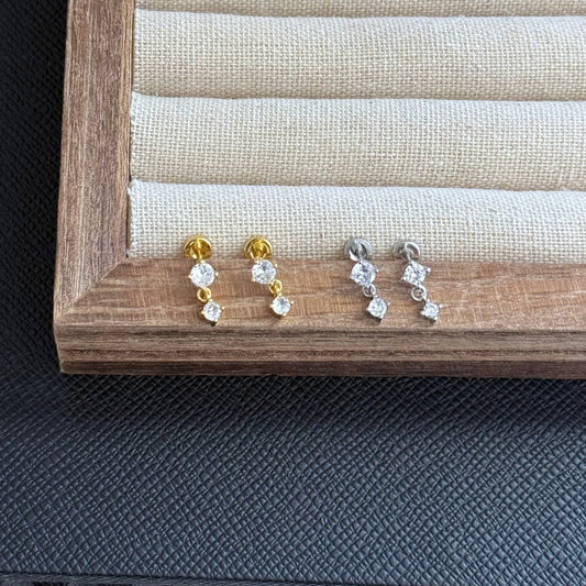 Pair of gold and silver stud earrings on a wooden display box.